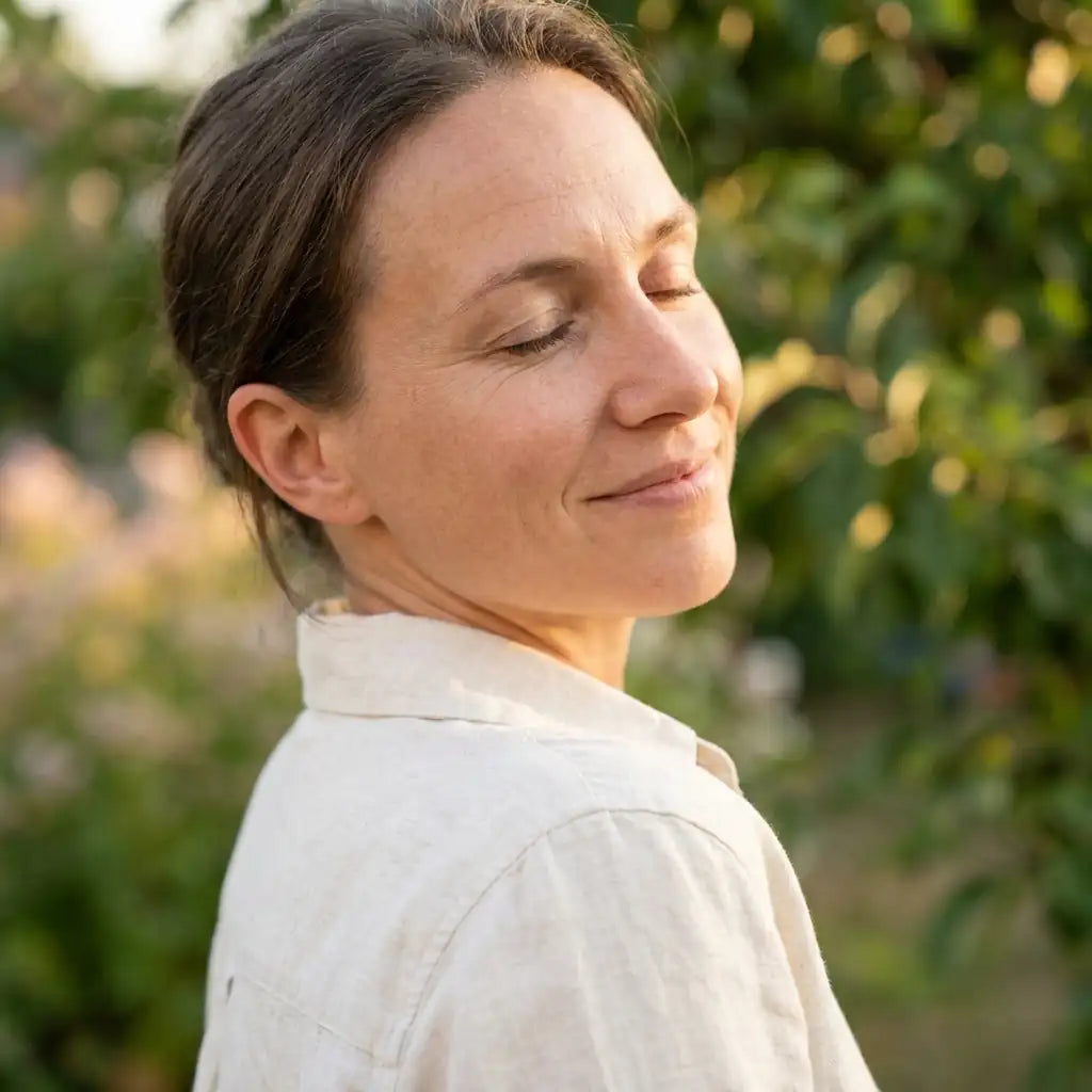 A woman smiling gently with her eyes closed in warm sunlight outdoors